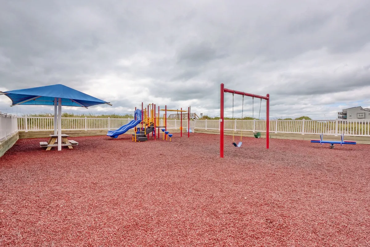 A colorful playground is shown with swings, a picnic table under a shade structure, and open play space. The inviting, family-friendly mood is enhanced by the presence of vibrant equipment and signs of children playing and family bonding.