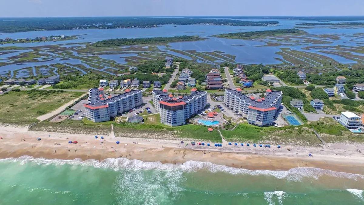 This exterior image captures the beachfront St. Regis buildings with a swimming pool in the foreground, colorful beach umbrellas, ocean waves, and families enjoying the outdoors. The lively atmosphere brings together the pool, beach, and communal outdoor spaces, all key features of family-oriented fun and relaxation.