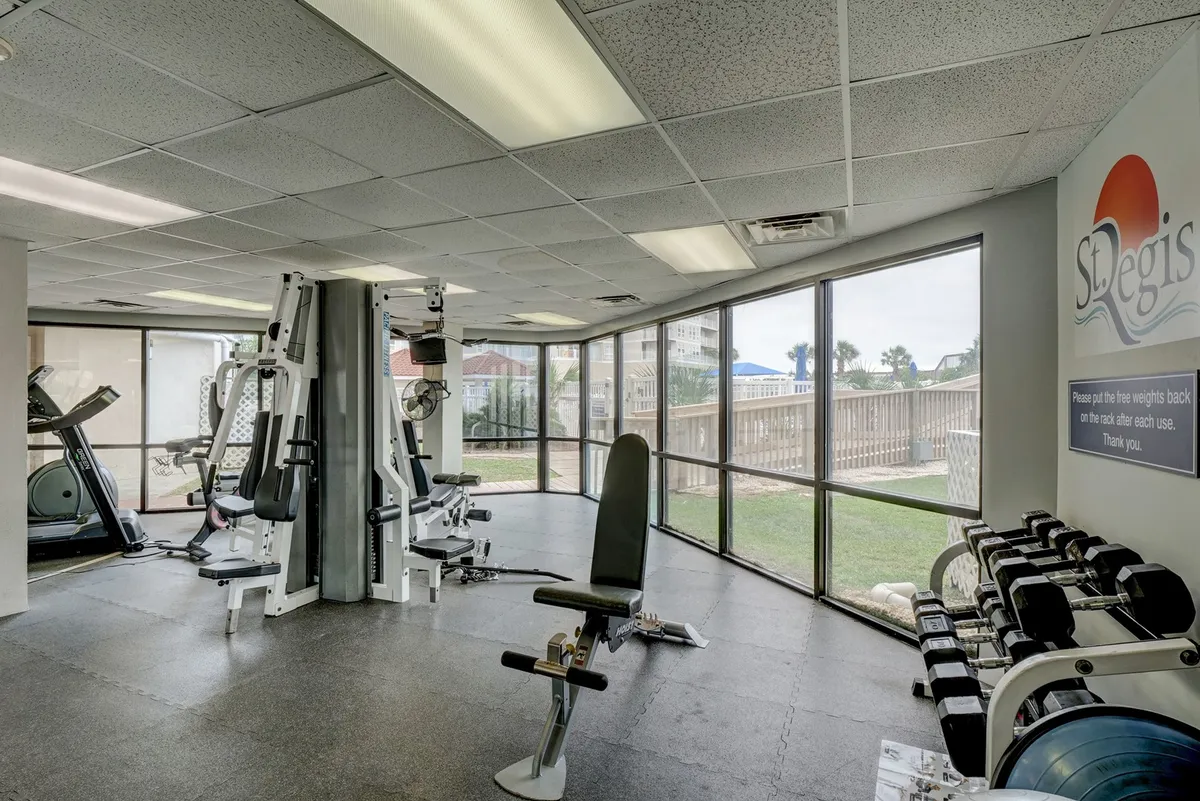 A bright, modern fitness center features exercise machines and large windows that let in natural light and offer partial views of the outdoors. The space feels motivating and inviting, ideal for wellness routines or post-beach workouts.