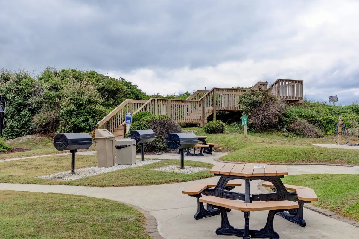 This exterior image depicts picnic tables, barbecue grills, a staircase, and lush greenery, creating a scene ready for family barbecues or relaxed outdoor meals. The communal setup is ideal for gatherings after a day of play.