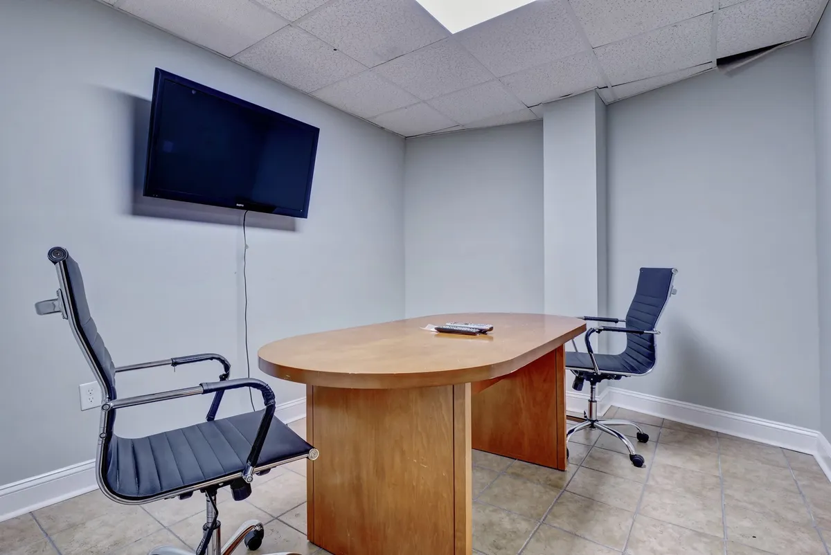 An interior shot of a business center-style space with a conference table, television, and chairs arranged for meetings or collaborative work. The clean, professional environment signals productive work sessions and business amenities available to guests.